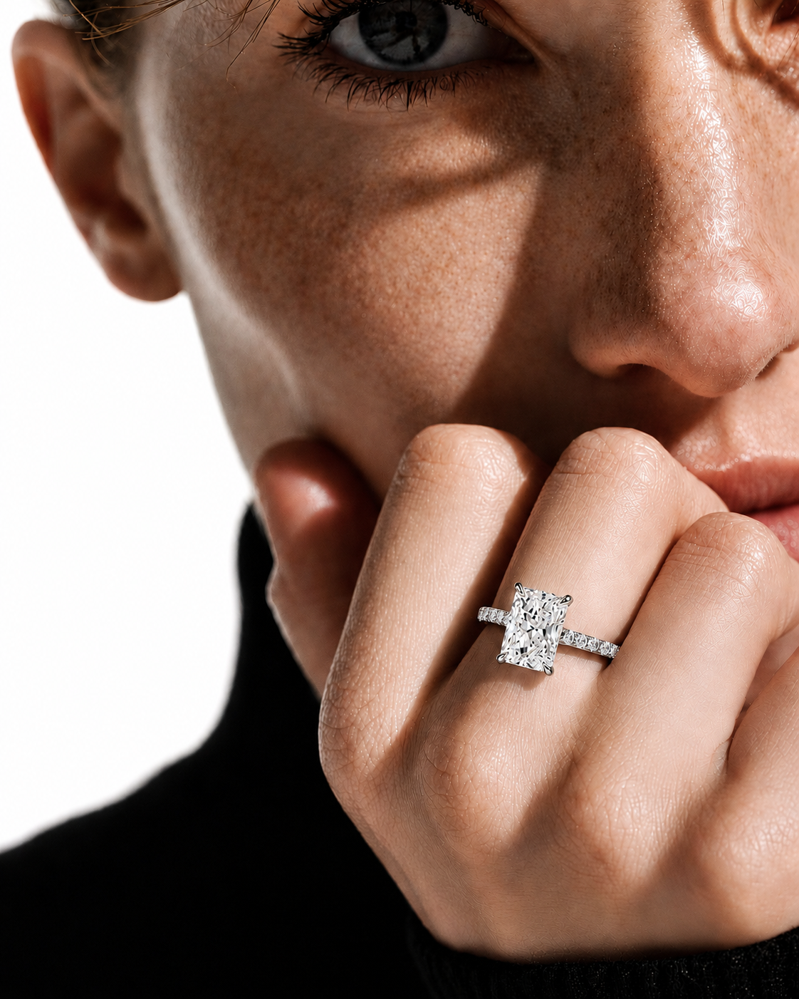 color_925_SIL,color_935_ARG,color_10K_WG, color_14K_WG &&
A close-up lifestyle shot of a model wearing a diamond engagement ring on her finger, with dramatic shadows across her face and a black turtleneck sweater.