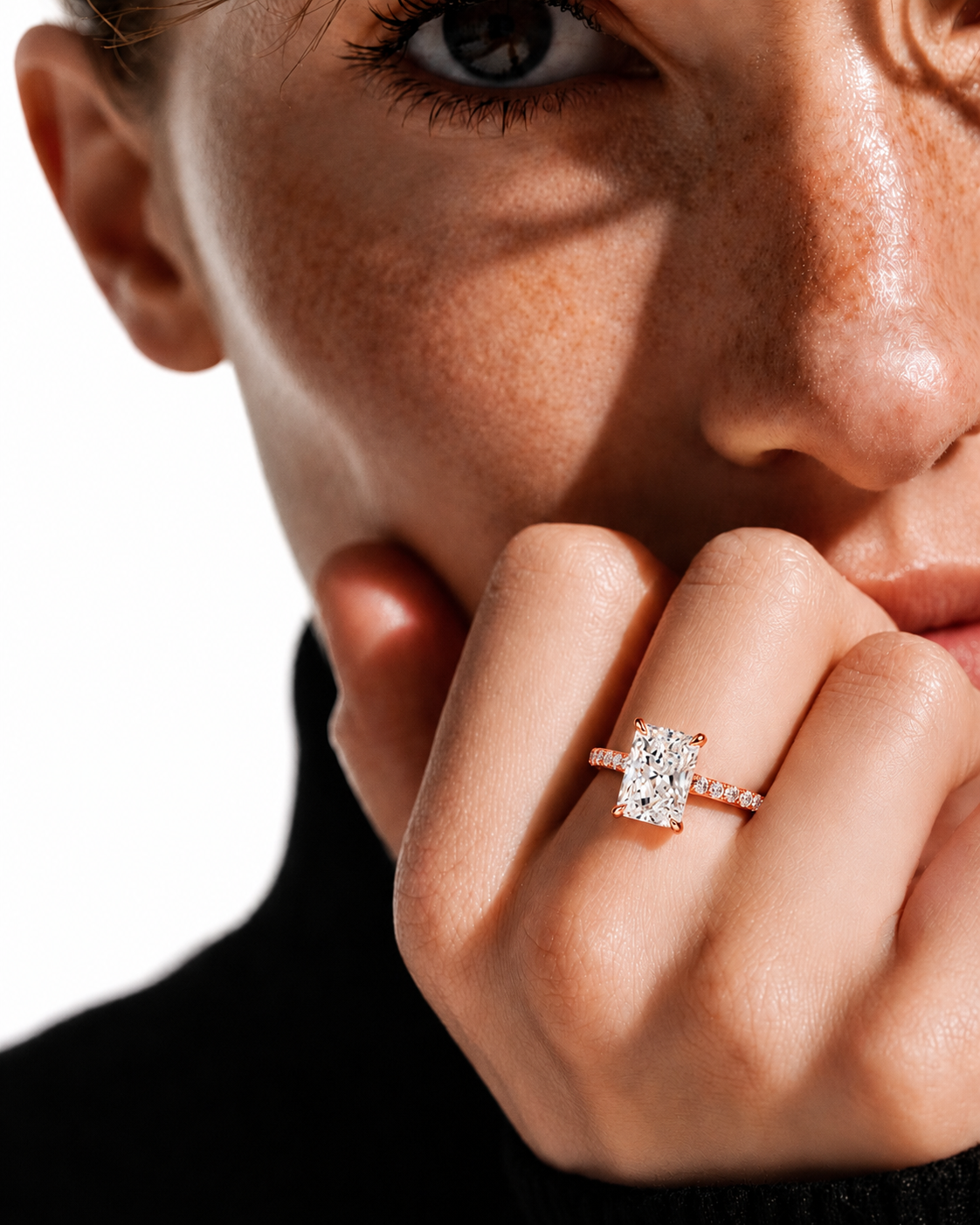 color_10K_RG, color_14K_RG &&
A close-up lifestyle shot of a model wearing a rose gold ring with a rectangular clear gemstone on her finger, set against a bright white background.