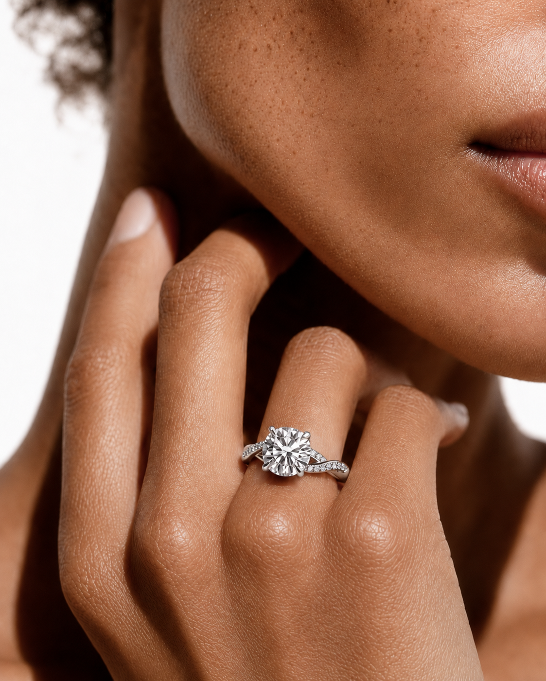color_925_SIL,color_935_ARG,color_10K_WG, color_14K_WG &&
A close-up lifestyle shot of a model wearing a silver-toned halo ring with a round-cut center stone and small side stones on her finger.