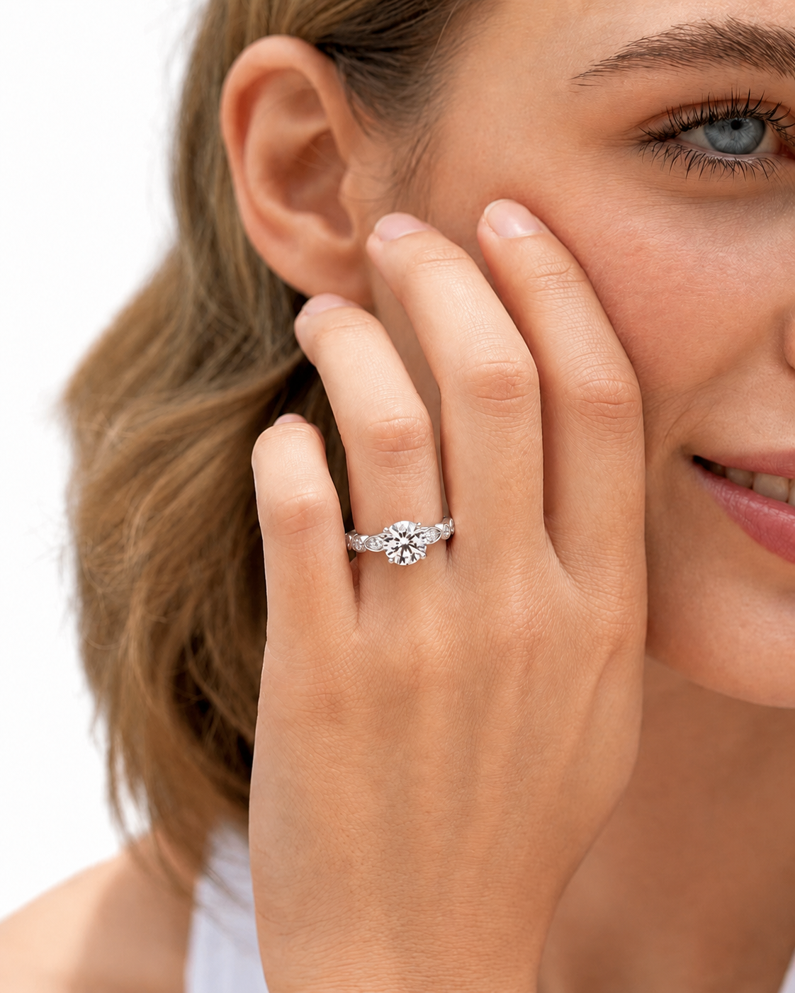 color_925_SIL,color_935_ARG,color_10K_WG, color_14K_WG &&
A close-up lifestyle shot of a woman wearing a rose gold diamond ring with a round-cut center stone and smaller side stones on her finger, with her hand resting against her cheek.