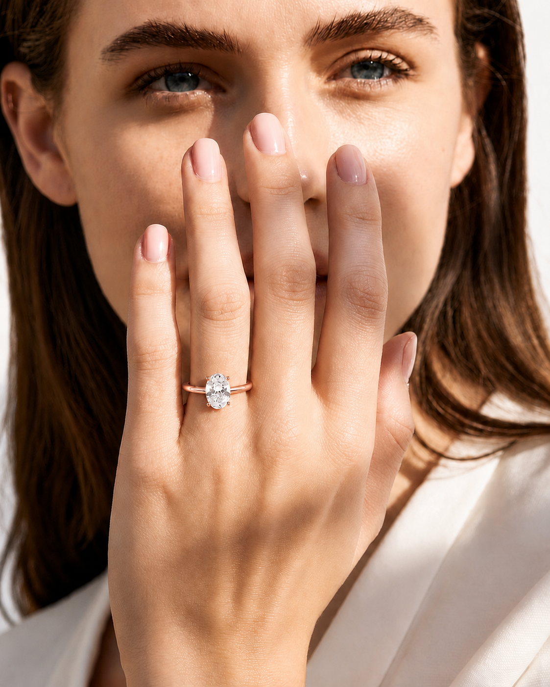 color_10K_RG, color_14K_RG &&A close-up lifestyle shot of a woman wearing a rose gold engagement ring with a round-cut clear gemstone on her finger, with her hand covering part of her face.