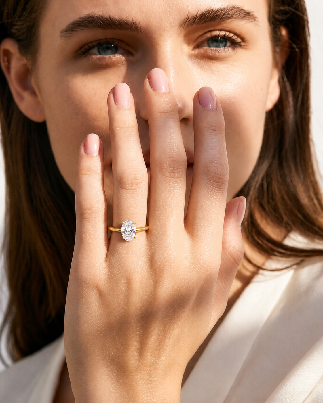 color_10K_YG, color_14K_YG &&A close-up lifestyle shot of a woman holding her hand near her face, wearing a yellow gold engagement ring with a round-cut clear gemstone.