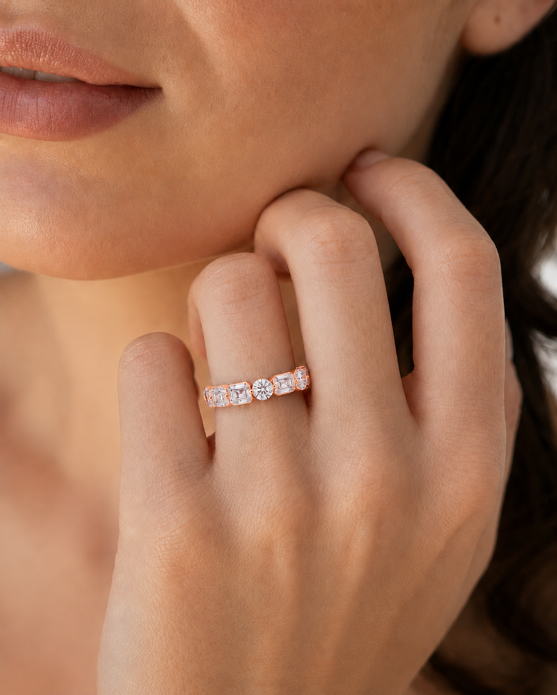 color_10K_RG, color_14K_RG &&	A close-up lifestyle shot of a woman's hand wearing a delicate rose gold eternity ring with clear round-cut gemstones.