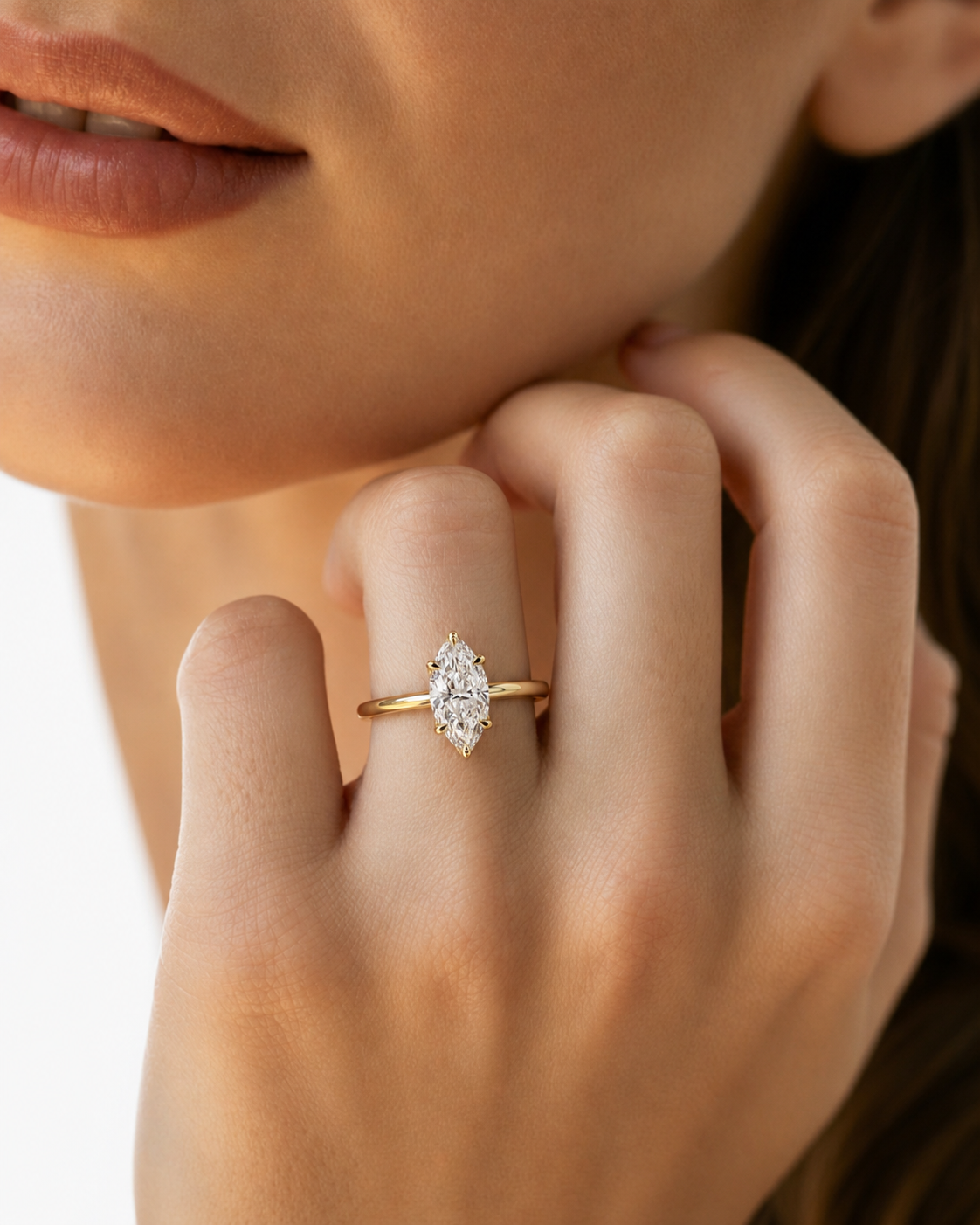 color_10K_YG, color_14K_YG &&A close-up of a woman's hand wearing a gold ring with a marquise-cut clear gemstone, set against her cheek and hair.