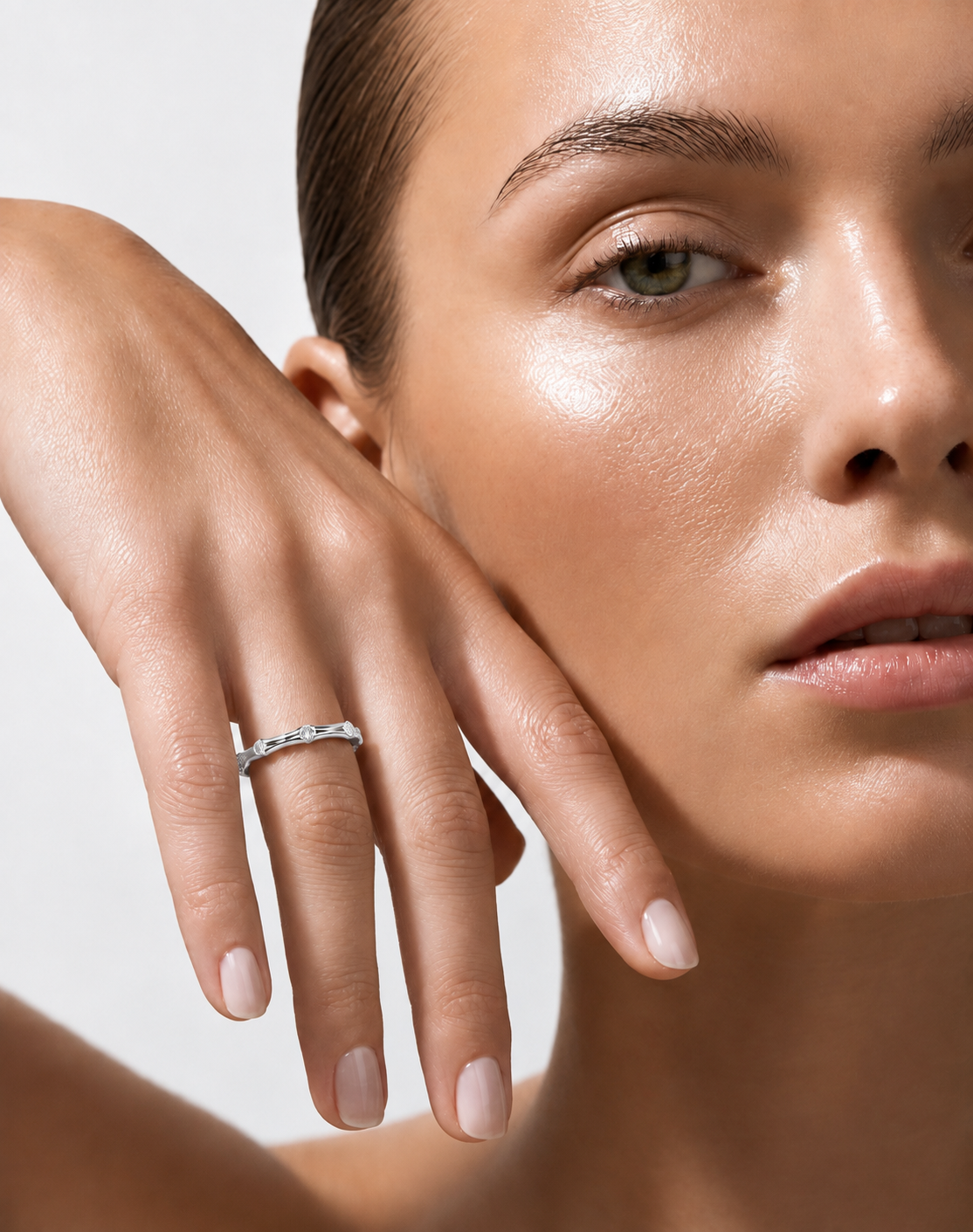 color_925_SIL,color_935_ARG,color_10K_WG, color_14K_WG &&	
A close-up lifestyle shot of a model wearing a delicate silver band ring with small clear stones on her ring finger, set against a clean, light gray background.