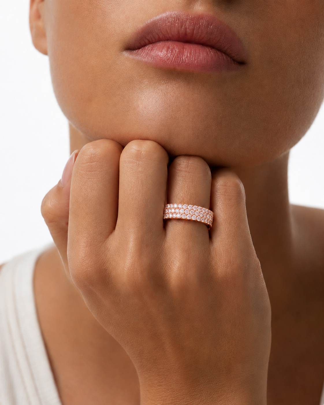 color_10K_RG, color_14K_RG &&	
A close-up lifestyle shot of a model wearing a rose gold eternity ring set with small clear stones on her ring finger, with her hand resting on her chin against a clean white background.