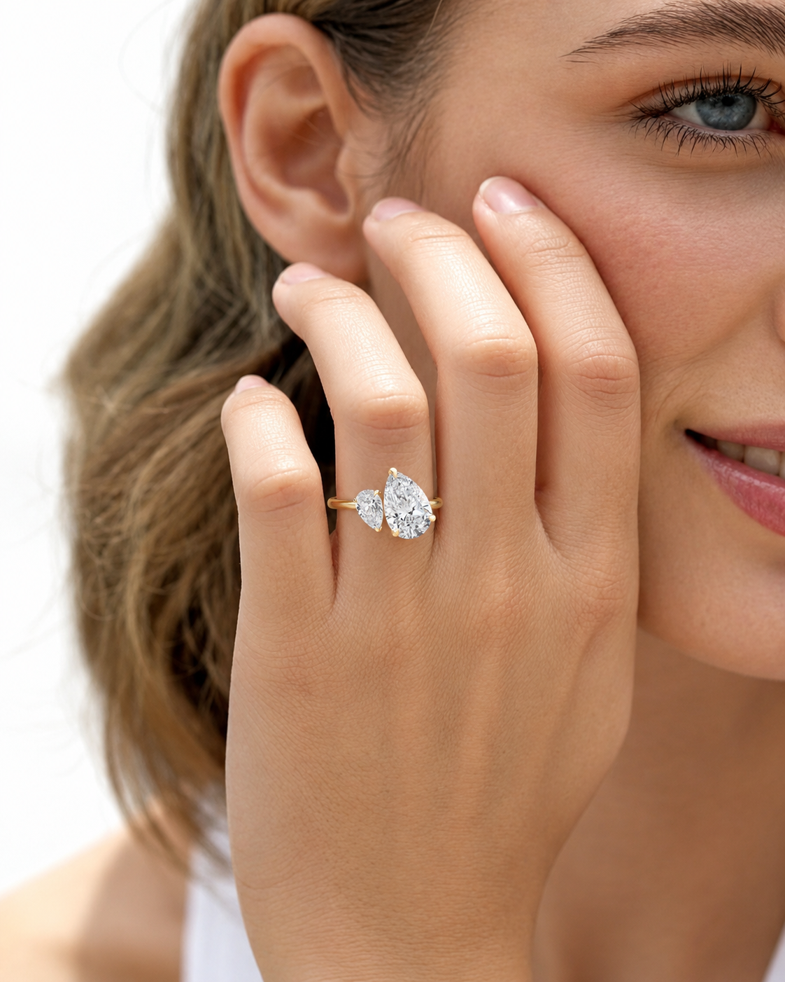 color_10K_YG, color_14K_YG &&A close-up lifestyle shot of a woman wearing a gold ring with a pear-cut diamond and a smaller heart-shaped diamond on her finger.