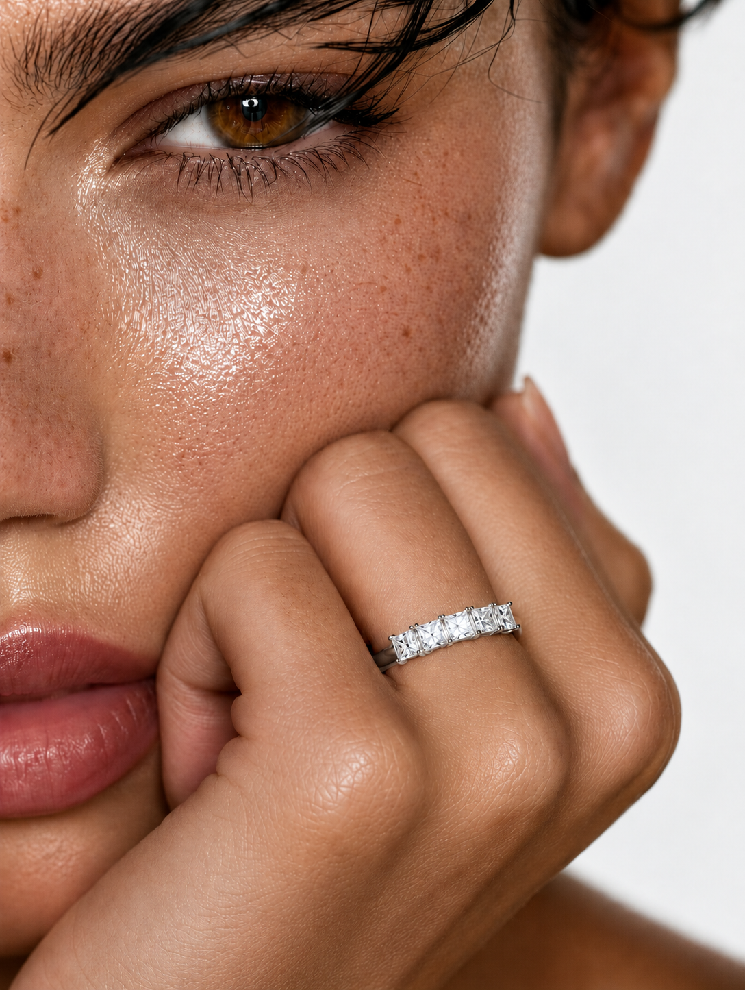 color_925_SIL,color_935_ARG,color_10K_WG, color_14K_WG &&	
A close-up of a model's face and hand wearing a sparkling diamond band ring on her index finger, set against a clean white background.