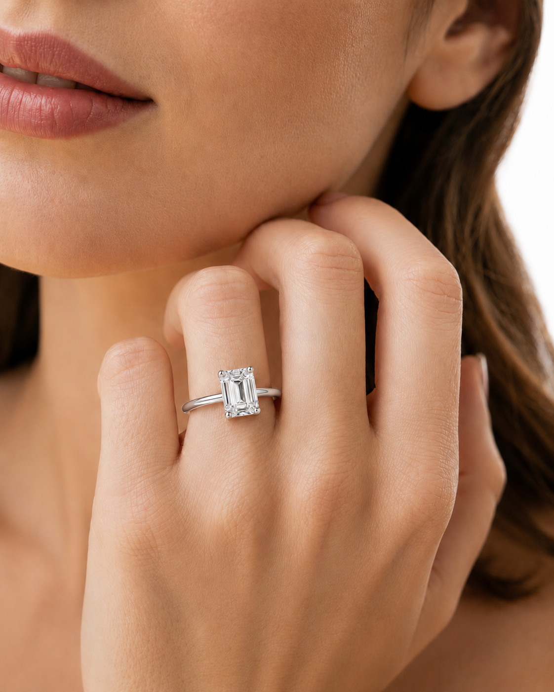 color_925_SIL,color_935_ARG,color_10K_WG, color_14K_WG &&A close-up lifestyle shot of a woman wearing a silver engagement ring with an emerald-cut diamond on her finger.