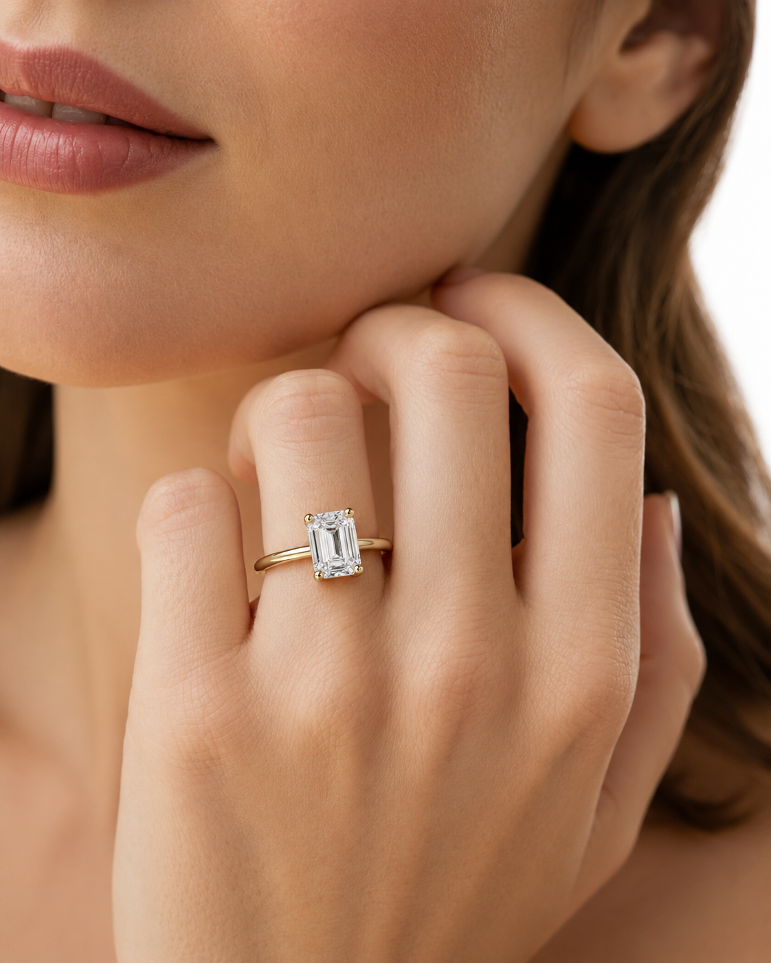 color_10K_YG, color_14K_YG &&A close-up lifestyle shot of a woman wearing a gold ring with an emerald-cut clear gemstone on her finger.