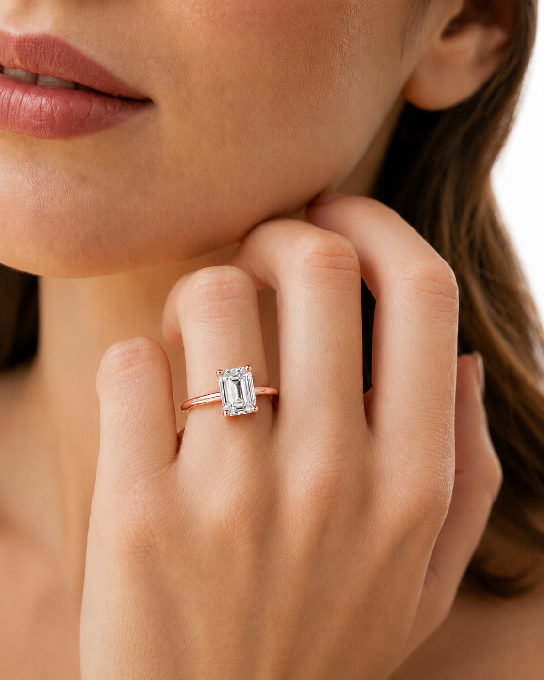 color_10K_RG, color_14K_RG &&A close-up lifestyle shot of a model wearing a rose gold ring with an emerald-cut clear gemstone on her finger.