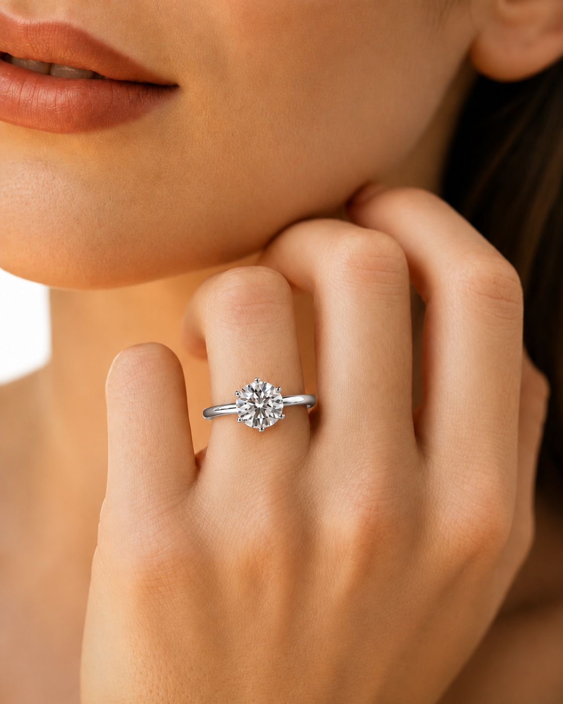 color_925_SIL,color_935_ARG,color_10K_WG, color_14K_WG &&A close-up lifestyle shot of a woman wearing a silver-toned diamond engagement ring on her finger, with her hand resting near her chin.