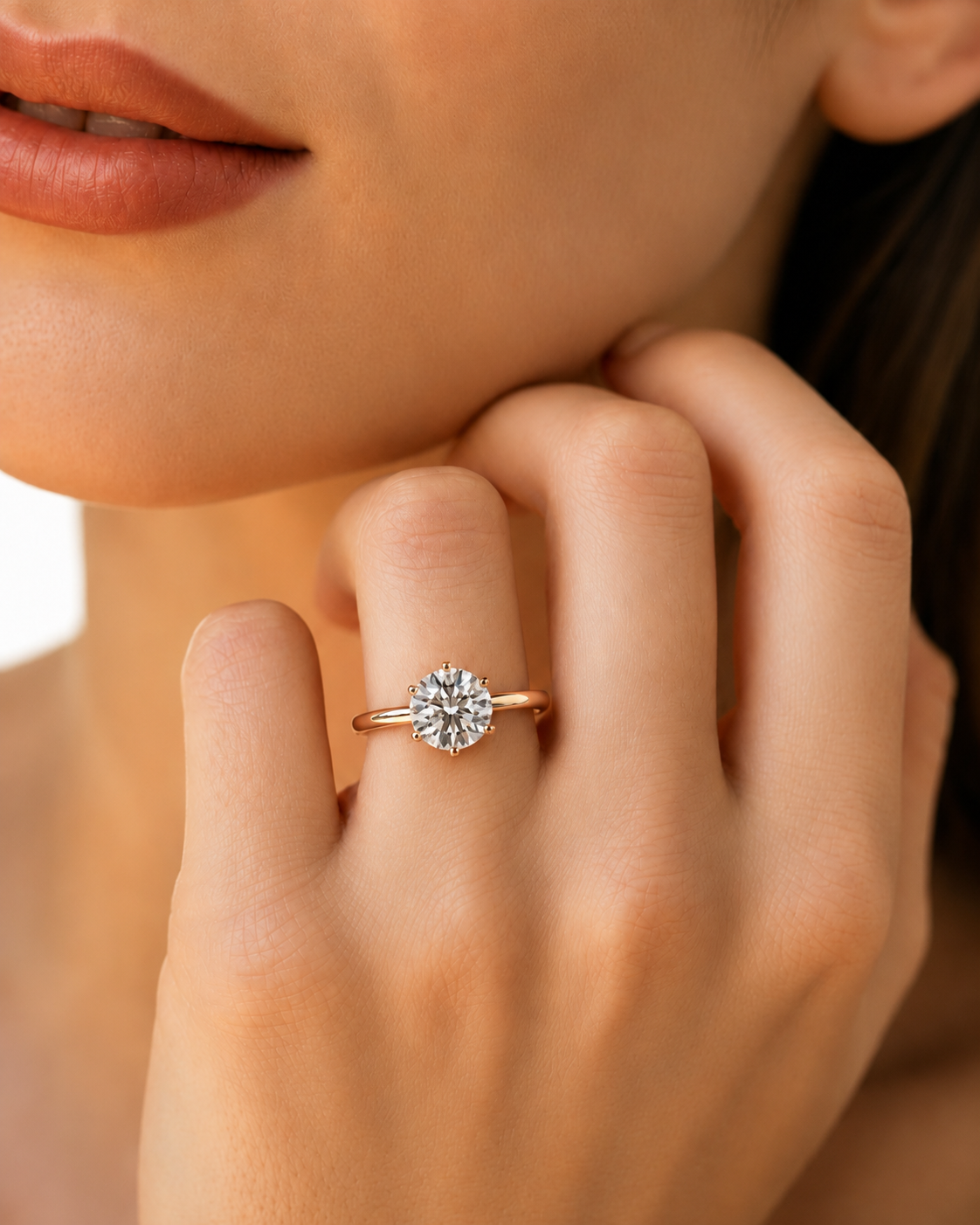color_10K_RG, color_14K_RG &&A close-up lifestyle shot of a model's hand wearing a rose gold engagement ring with a round-cut diamond. The background is a soft, warm beige skin tone.