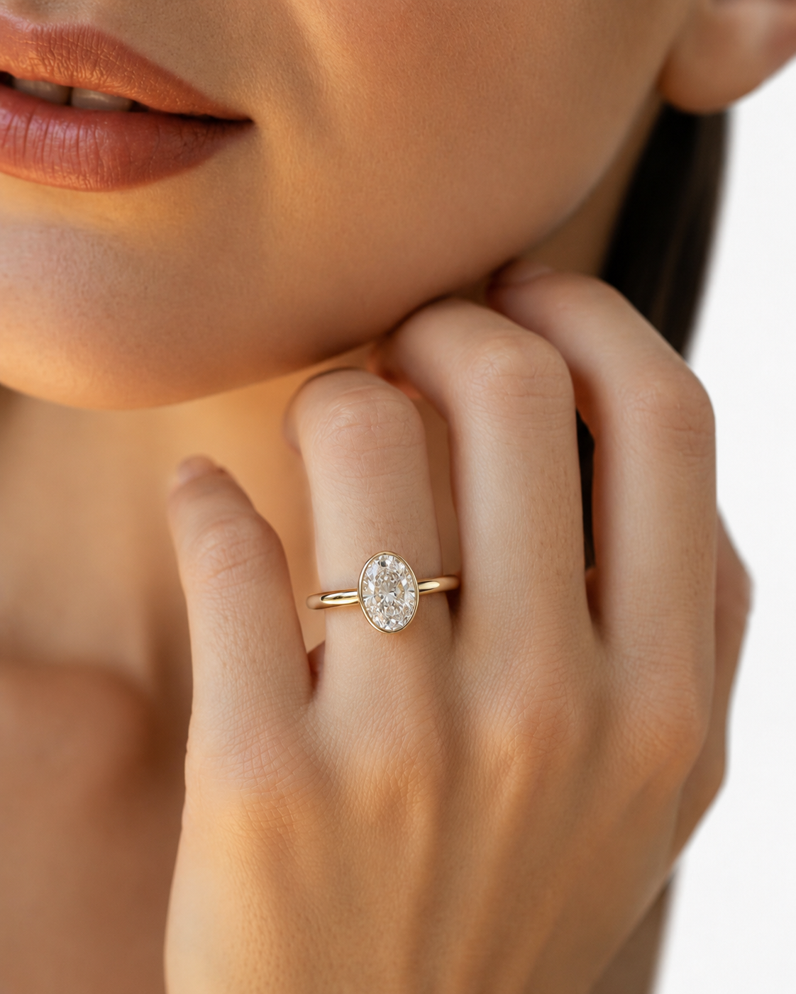 color_10K_YG, color_14K_YG &&A close-up lifestyle shot of a model wearing a gold ring with an oval-cut clear gemstone on her finger.