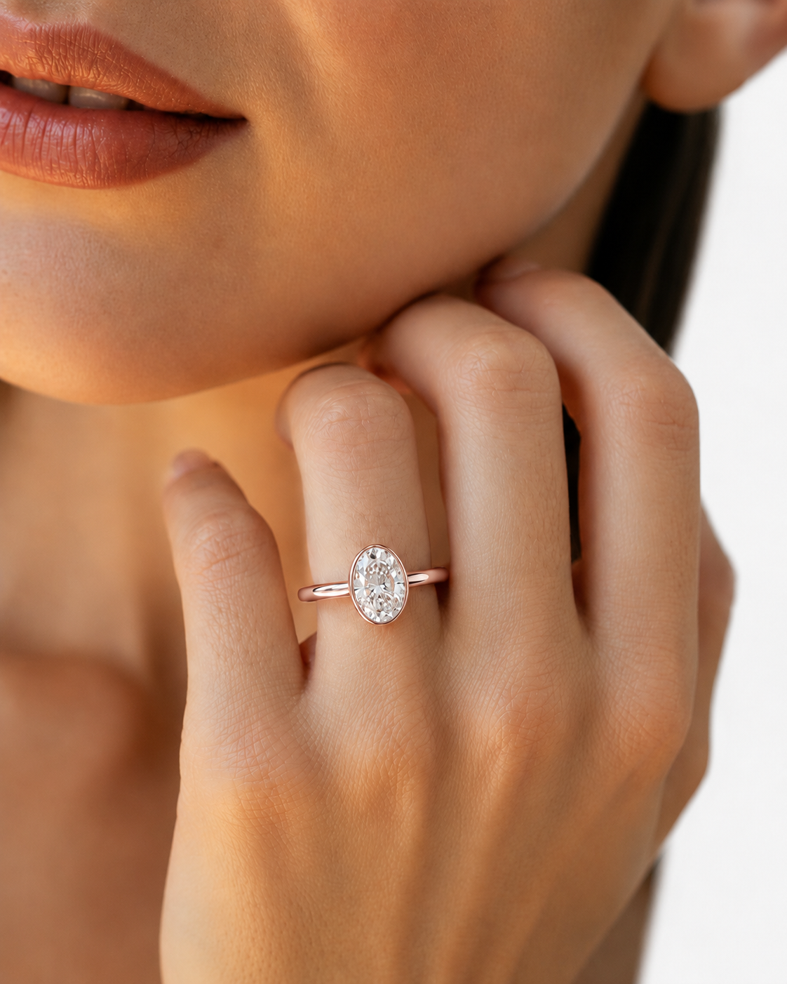 color_10K_RG, color_14K_RG &&A close-up lifestyle shot of a model wearing a rose gold ring with an oval-cut clear gemstone in a bezel setting on her finger.