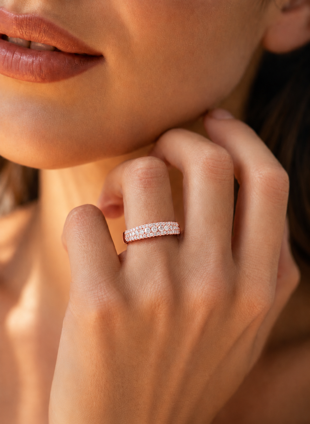 color_10K_RG, color_14K_RG &&	
A close-up lifestyle shot of a model wearing a thin rose gold eternity ring set with small clear stones on her finger.