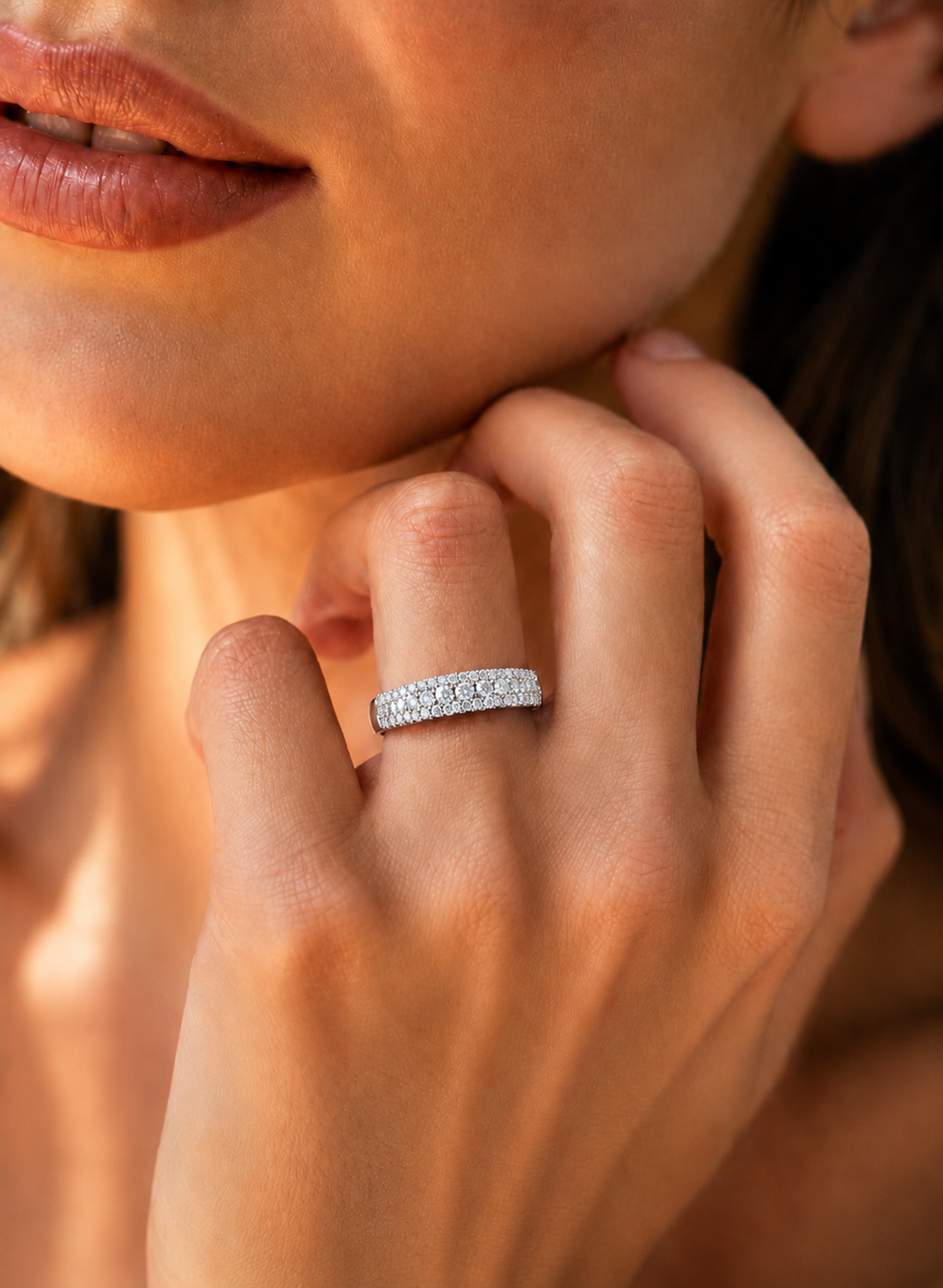 color_925_SIL,color_935_ARG,color_10K_WG, color_14K_WG &&	
A close-up lifestyle shot of a woman's hand wearing a silver band ring set with small clear stones, against a warm, softly blurred background.