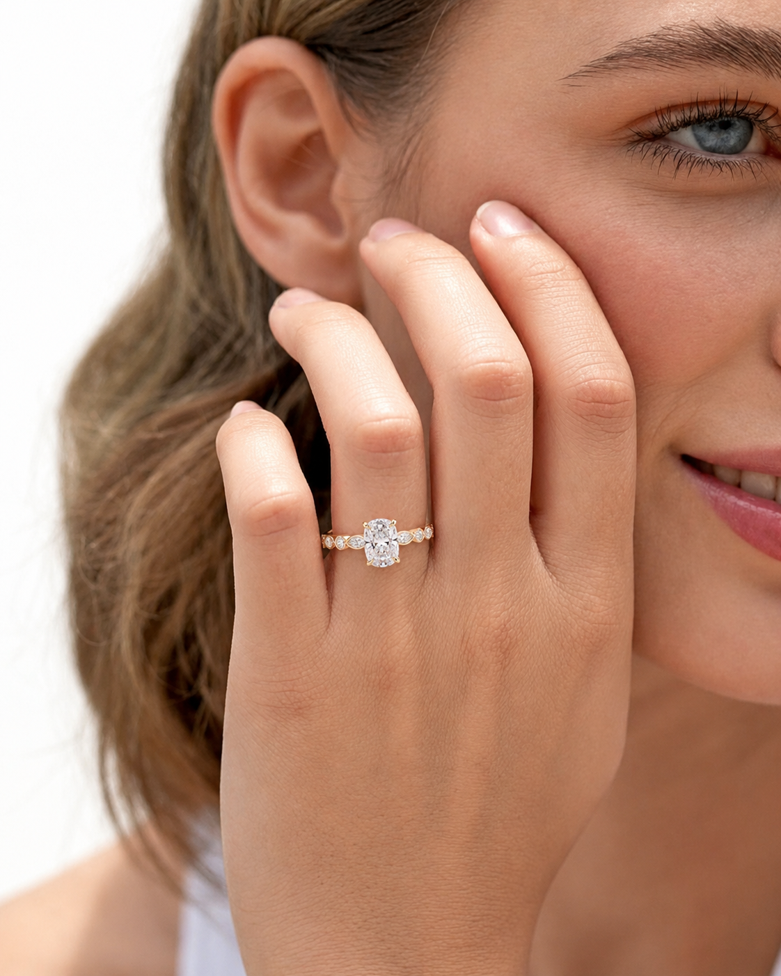 color_10K_YG, color_14K_YG &&
A close-up lifestyle shot of a woman wearing a diamond engagement ring on her finger, with her hand resting against her cheek against a clean white background.