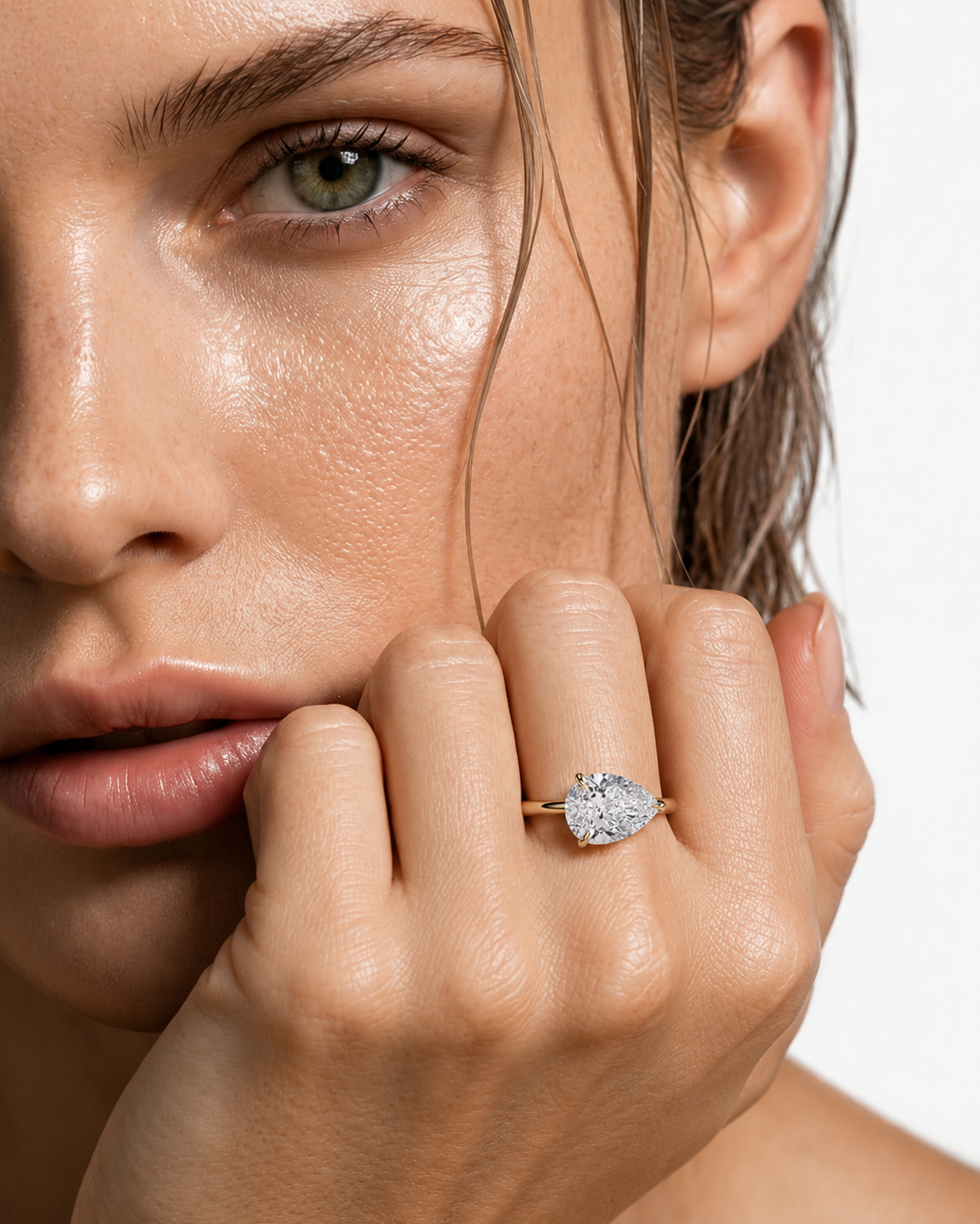 color_10K_YG, color_14K_YG &&
A close-up lifestyle shot of a model wearing a heart-shaped diamond engagement ring on a gold band, with her hand resting near her chin against a clean white background.