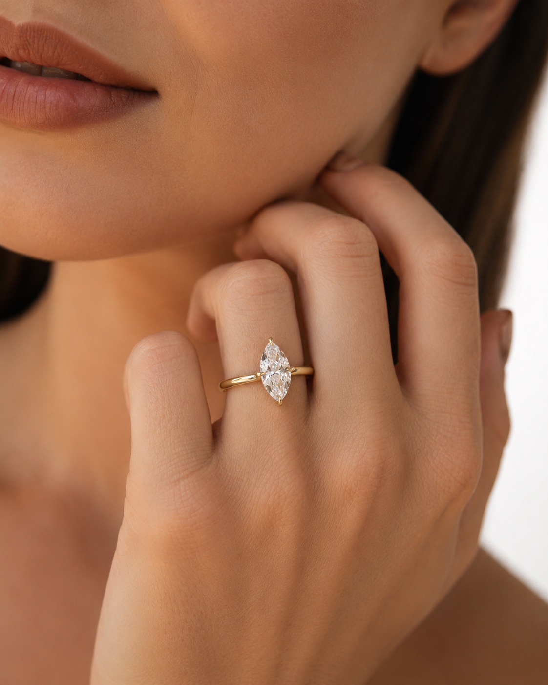 color_10K_YG, color_14K_YG &&A close-up lifestyle shot of a model wearing a yellow gold ring with a marquise-cut clear gemstone on her finger.