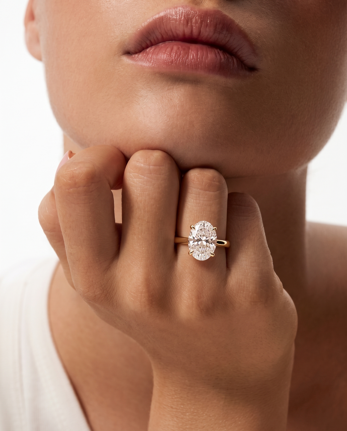 color_10K_YG, color_14K_YG &&A close-up lifestyle shot of a model wearing a gold ring with a large, round-cut clear gemstone. The model's hand, lips, and chin are visible against a clean white background.