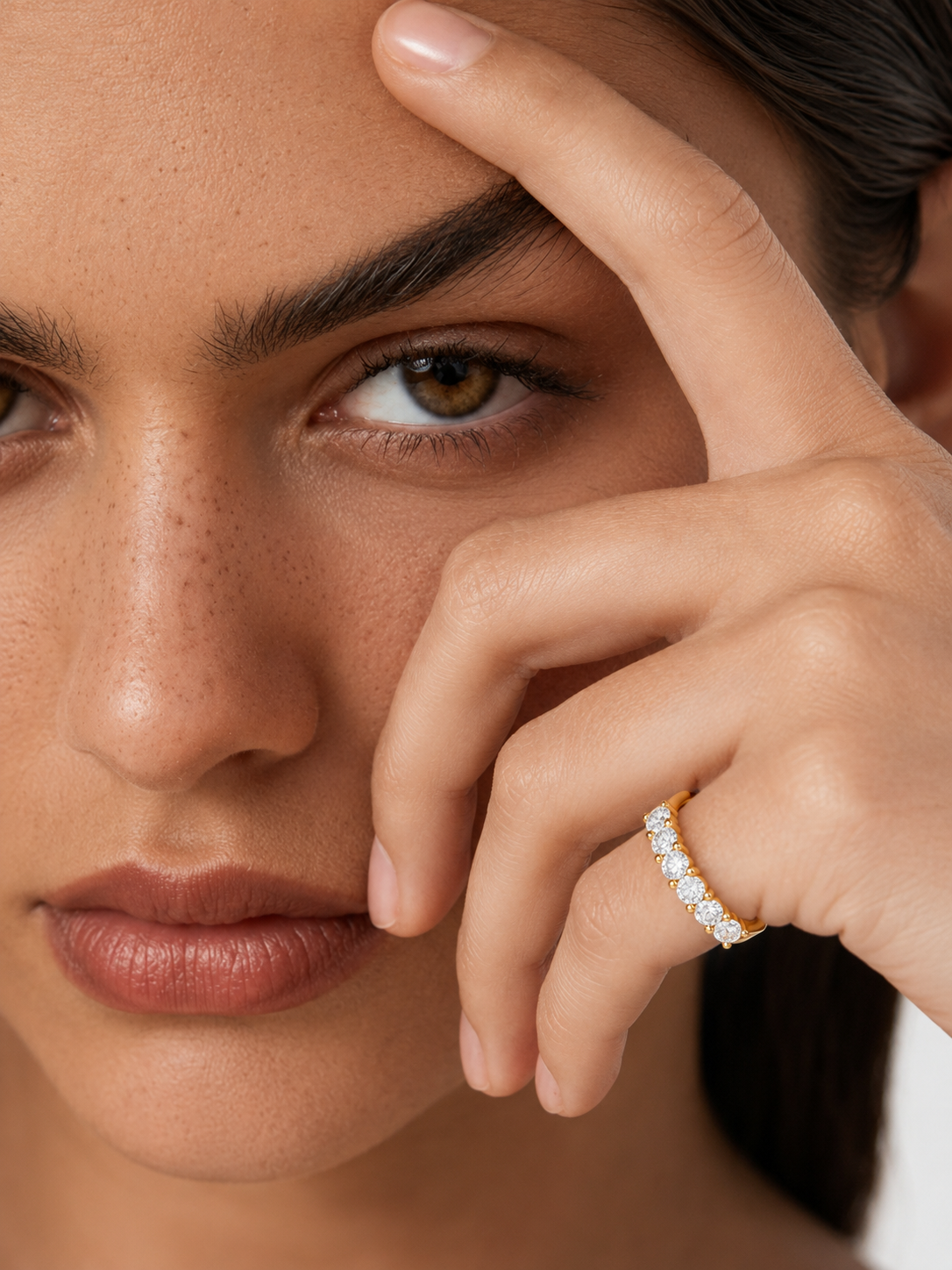 color_10K_YG, color_14K_YG &&Close-up of a woman's face and hand wearing a delicate gold ring set with small clear stones on her ring finger.