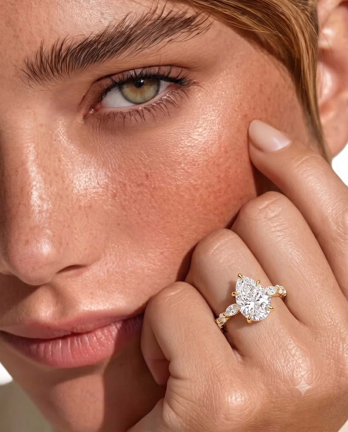 color_10K_YG, color_14K_YG &&Close-up of a model's face and hand wearing a gold ring with a large clear marquise-cut center stone and smaller side stones.