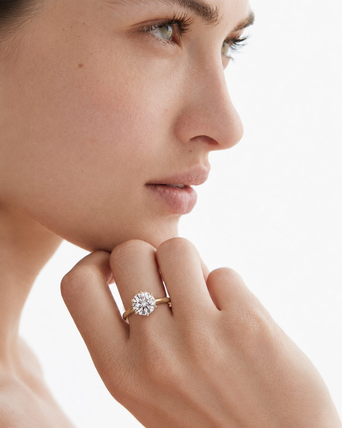 color_10K_YG, color_14K_YG &&A close-up side profile of a woman wearing a delicate gold ring with a round-cut clear gemstone on her finger, set against a bright white background.