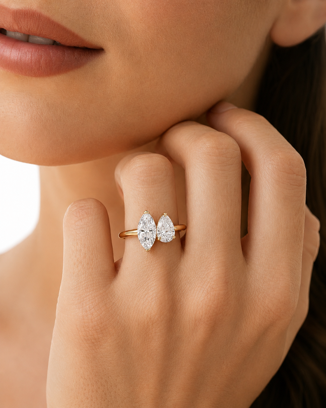 color_10K_YG, color_14K_YG &&A close-up lifestyle shot of a model wearing a delicate gold ring with two pear-cut clear gemstones set in a bow-like shape on her finger.