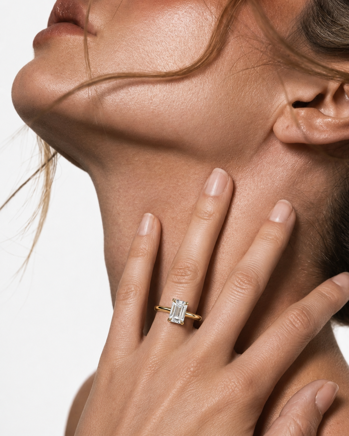 color_10K_YG, color_14K_YG &&A close-up lifestyle shot of a model wearing a gold ring with a rectangular emerald-cut clear gemstone on her finger, with her hand resting on her neck against a white background.