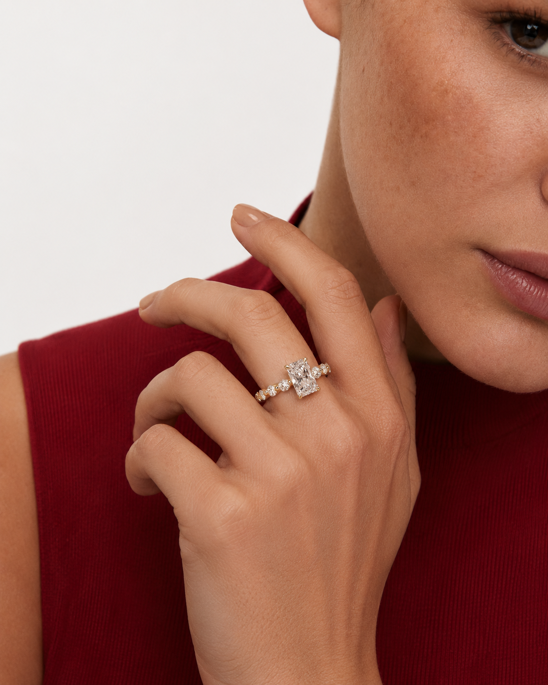color_10K_YG, color_14K_YG &&A close-up lifestyle shot of a woman wearing a delicate silver ring with a central clear gemstone and smaller side stones, set against a clean white background and a red ribbed top.
