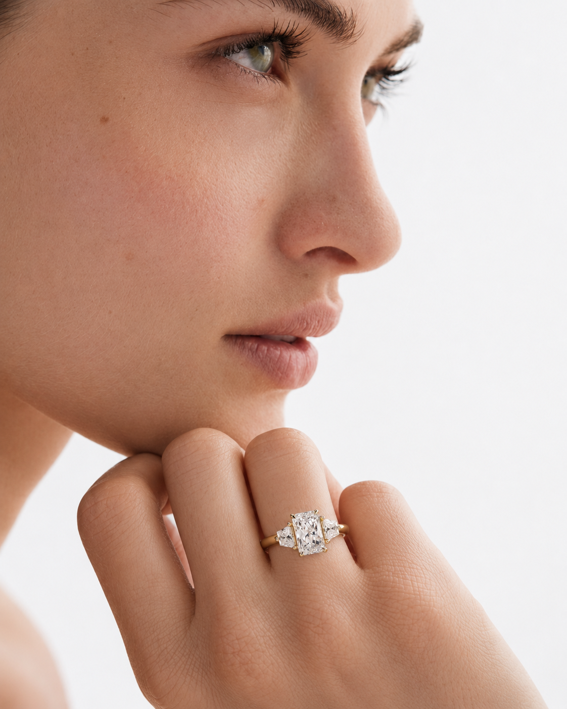 color_10K_YG, color_14K_YG &&A close-up lifestyle shot of a model wearing a yellow gold ring with a rectangular cluster of clear gemstones on her finger, set against a clean white background.