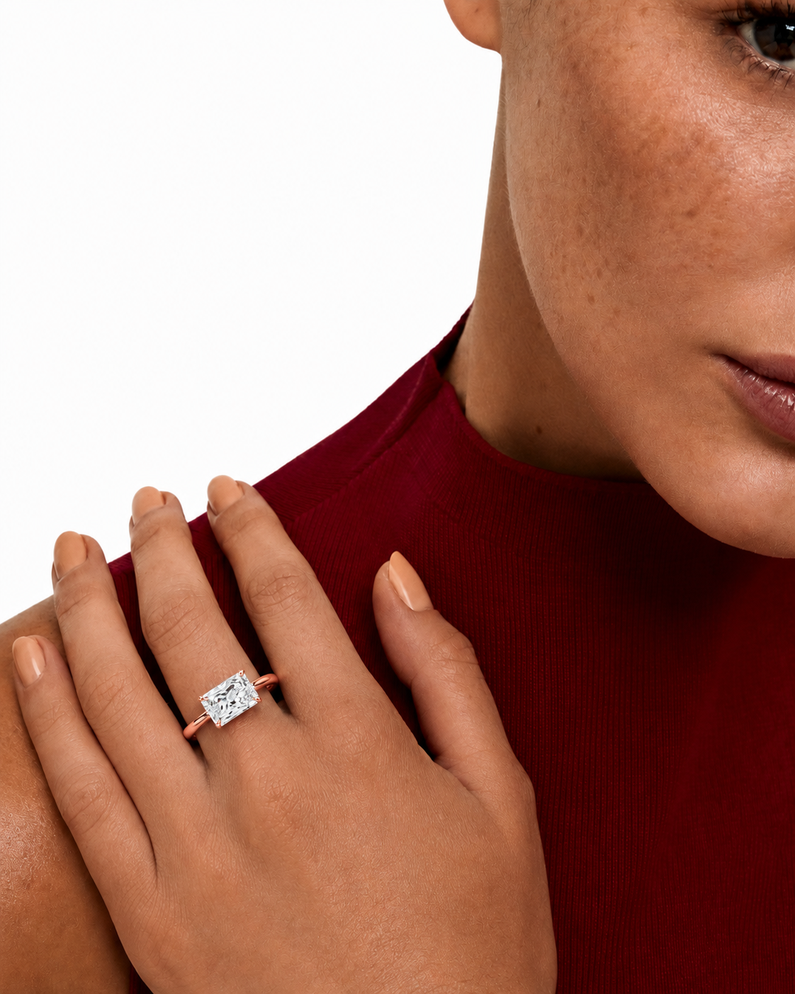 color_10K_RG, color_14K_RG &&
A close-up lifestyle shot of a model wearing a rose gold ring with a square-cut clear gemstone on her finger, paired with a deep red ribbed top against a white background.