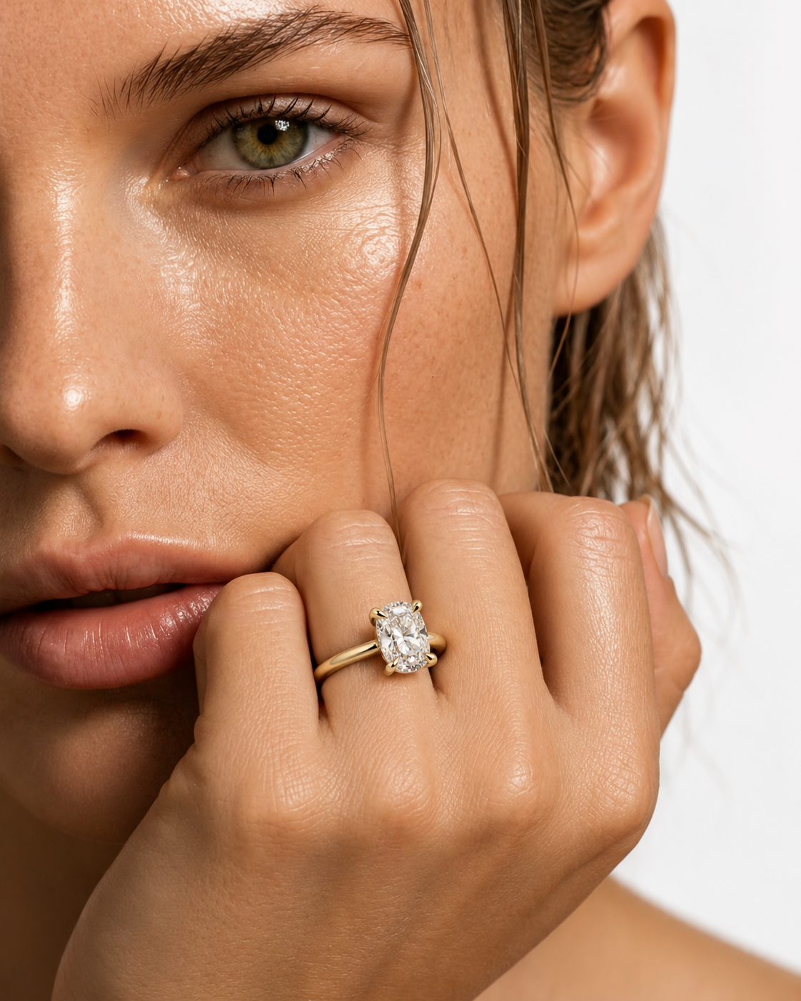 color_10K_YG, color_14K_YG &&A close-up of a woman's face and hand wearing a yellow gold ring with a rectangular clear gemstone on the ring finger, set against a clean white background.