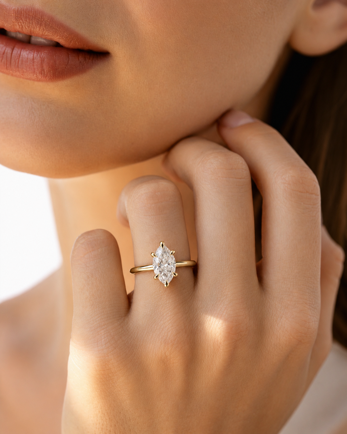 color_10K_YG, color_14K_YG &&A close-up lifestyle shot of a model wearing a gold ring with a marquise-cut clear gemstone on her finger.