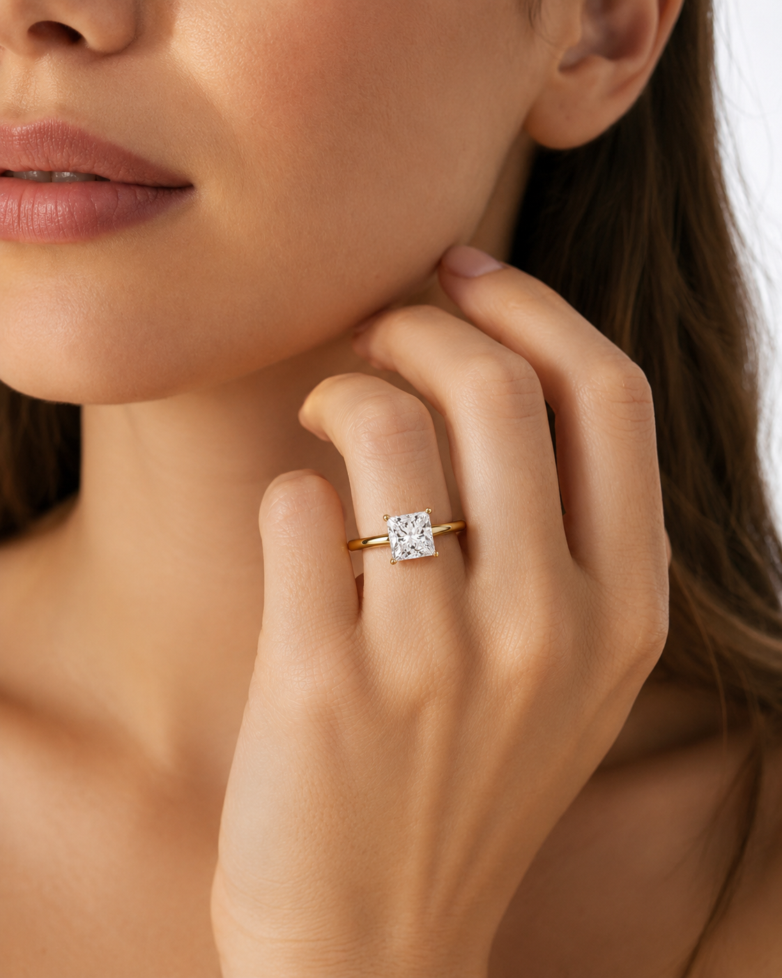 color_10K_YG, color_14K_YG &&A close-up lifestyle shot of a model wearing a yellow gold ring with a square-cut clear gemstone on her finger.
