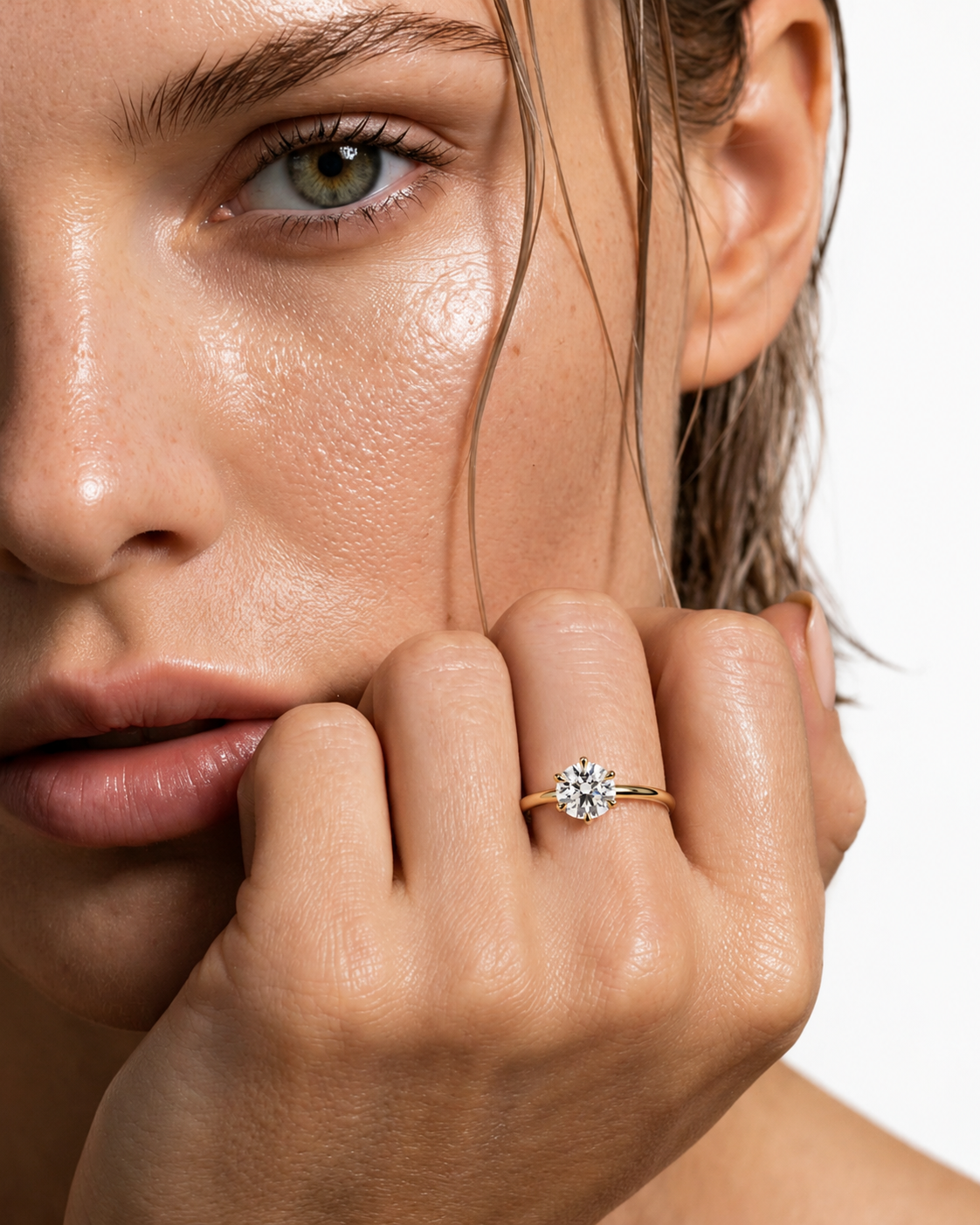 color_10K_YG, color_14K_YG &&A close-up lifestyle shot of a model wearing a yellow gold ring with a round-cut clear gemstone on her finger, set against a clean white background.