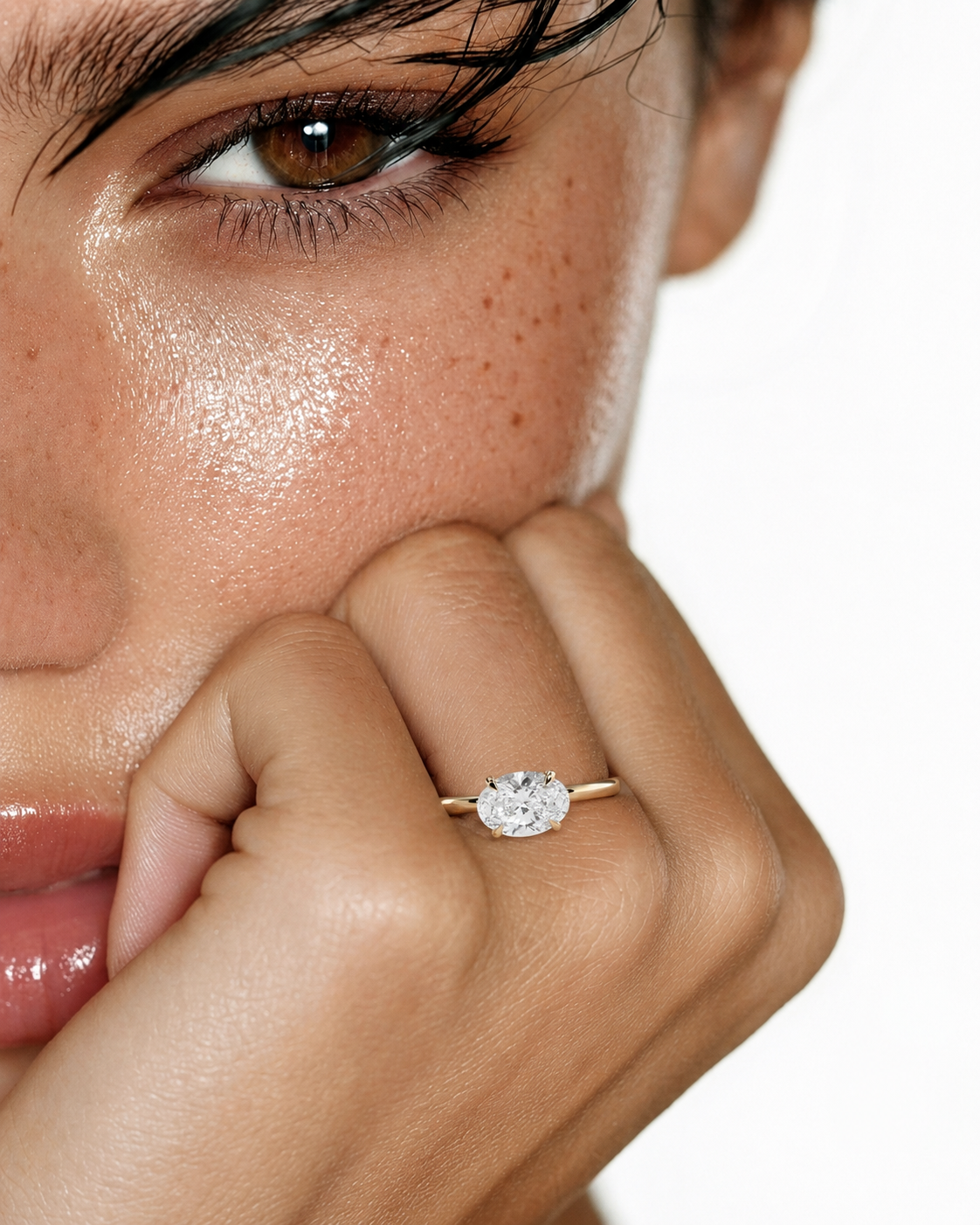color_10K_YG, color_14K_YG &&A close-up lifestyle shot of a model wearing a classic solitaire engagement ring with a round brilliant-cut diamond on a thin yellow gold band. The model's face and hand are shown against a clean white background.
