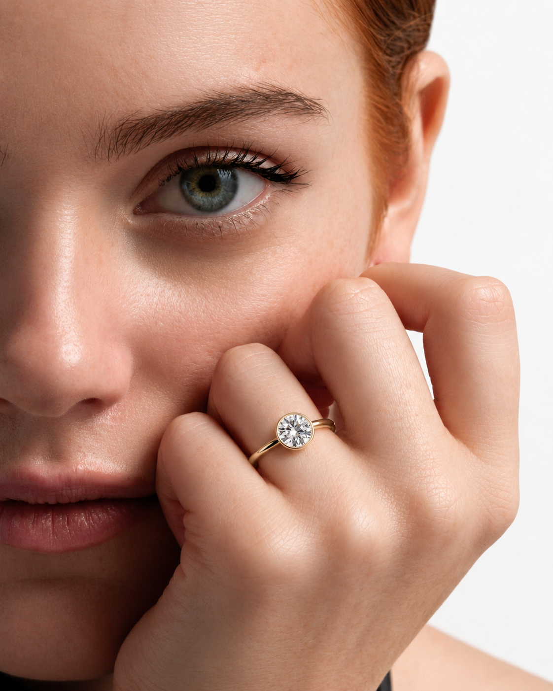 color_10K_YG, color_14K_YG &&A close-up lifestyle shot of a woman with red hair wearing a gold engagement ring with a round-cut diamond on her ring finger, set against a clean white background.