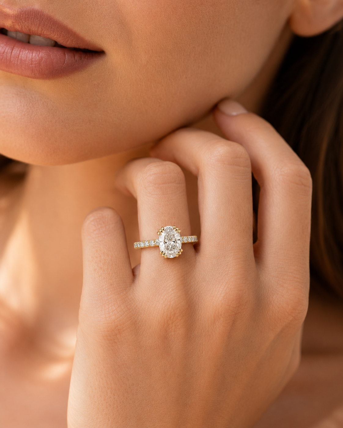 color_10K_YG, color_14K_YG &&A close-up lifestyle shot of a woman's hand wearing a silver ring with a halo-style oval diamond setting and a small pavé band.