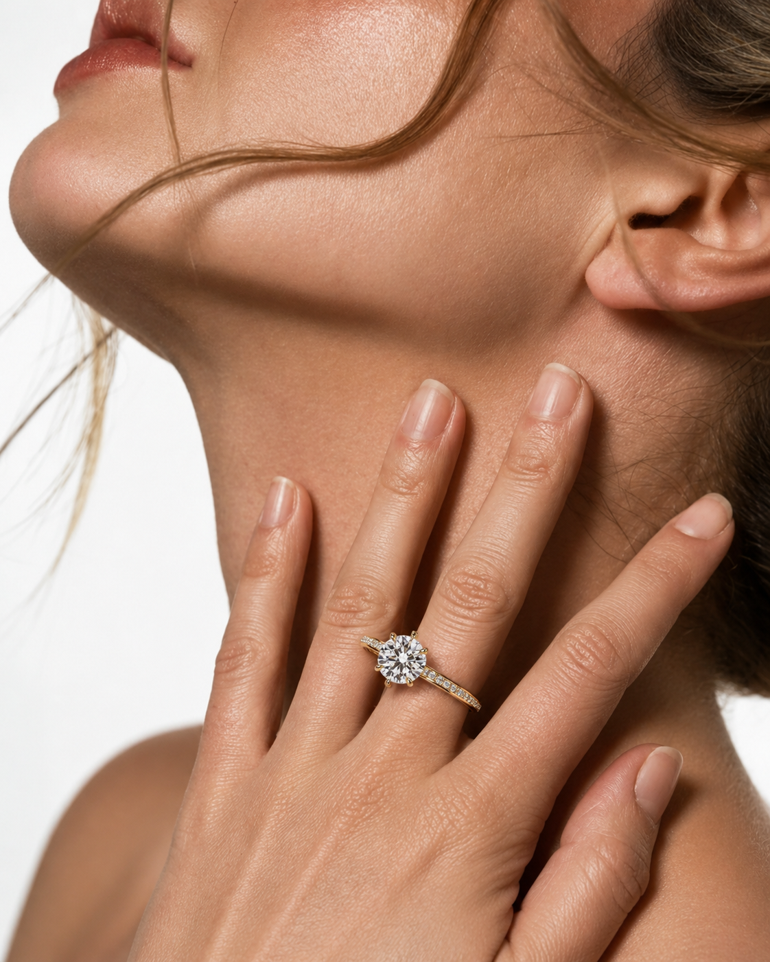 color_10K_YG, color_14K_YG &&A close-up lifestyle shot of a woman's hand resting on her neck, wearing a silver-toned diamond engagement ring with a round-cut center stone and small side stones.