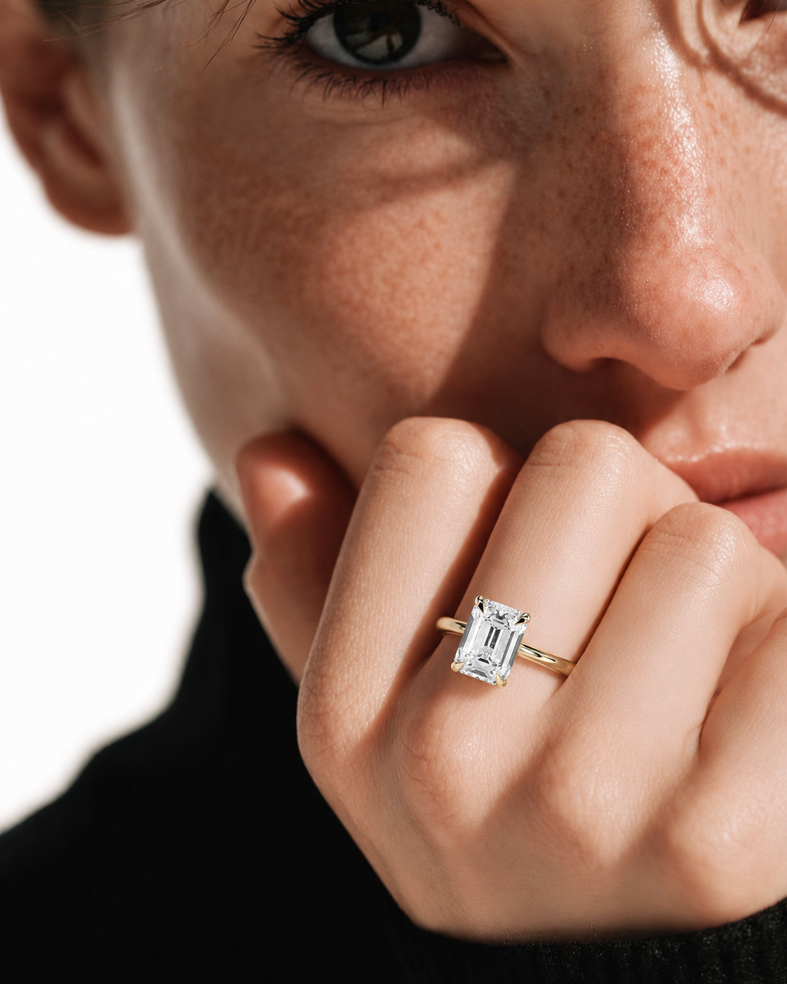 color_10K_YG, color_14K_YG &&A close-up lifestyle shot of a model wearing a yellow gold ring with a rectangular baguette-cut clear gemstone. The ring is shown on the model's finger, with dramatic shadows across her face and hand.