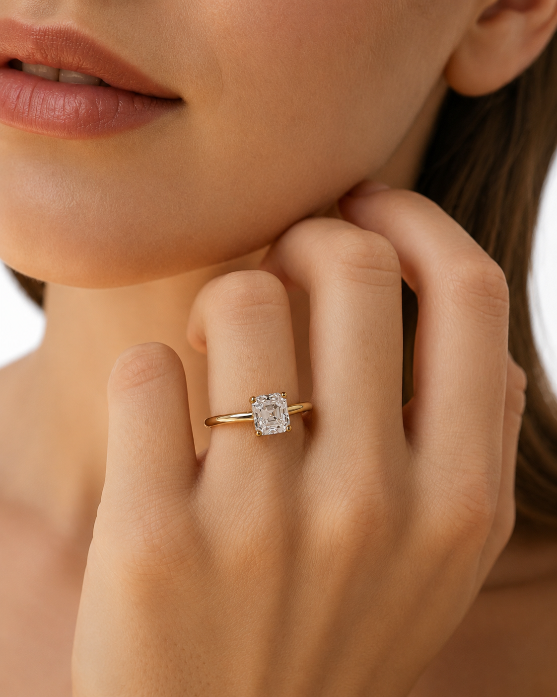 color_10K_YG, color_14K_YG &&	
A close-up lifestyle shot of a model wearing a gold engagement ring with a rectangular clear gemstone on her finger.