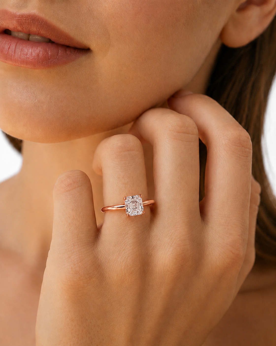 color_10K_RG, color_14K_RG &&	A close-up lifestyle shot of a model wearing a gold engagement ring with a rectangular clear gemstone on her finger.