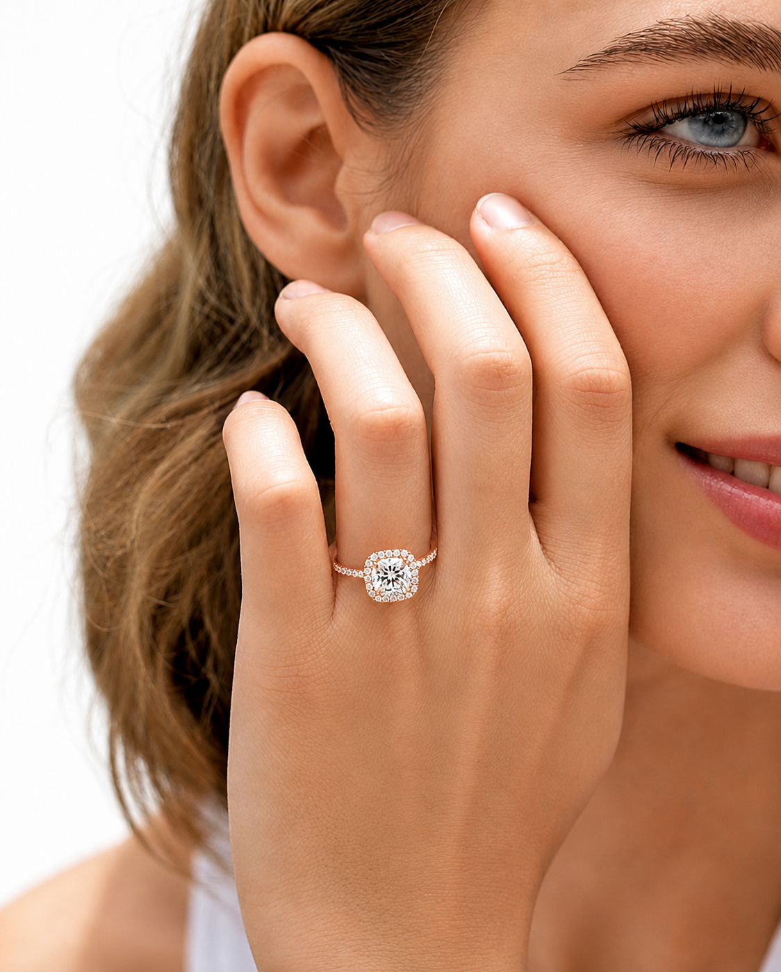 color_10K_RG, color_14K_RG &&	A close-up lifestyle shot of a woman wearing a diamond halo ring on her finger, with her hand resting against her cheek against a clean white background.