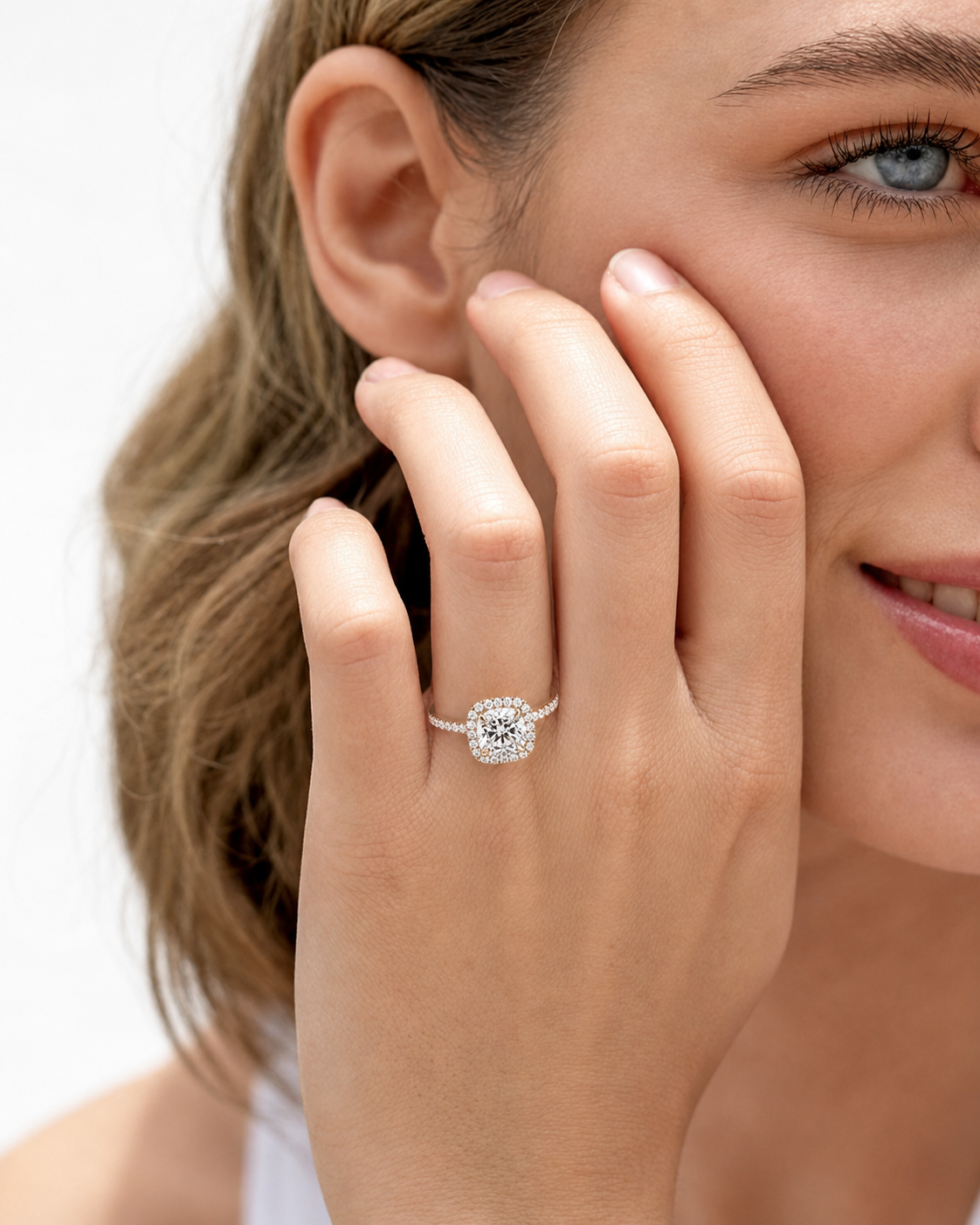 color_10K_YG, color_14K_YG &&	
A close-up lifestyle shot of a woman wearing a silver halo ring with a round-cut clear center stone and surrounding pave-set stones on her finger, with her hand resting against her cheek.