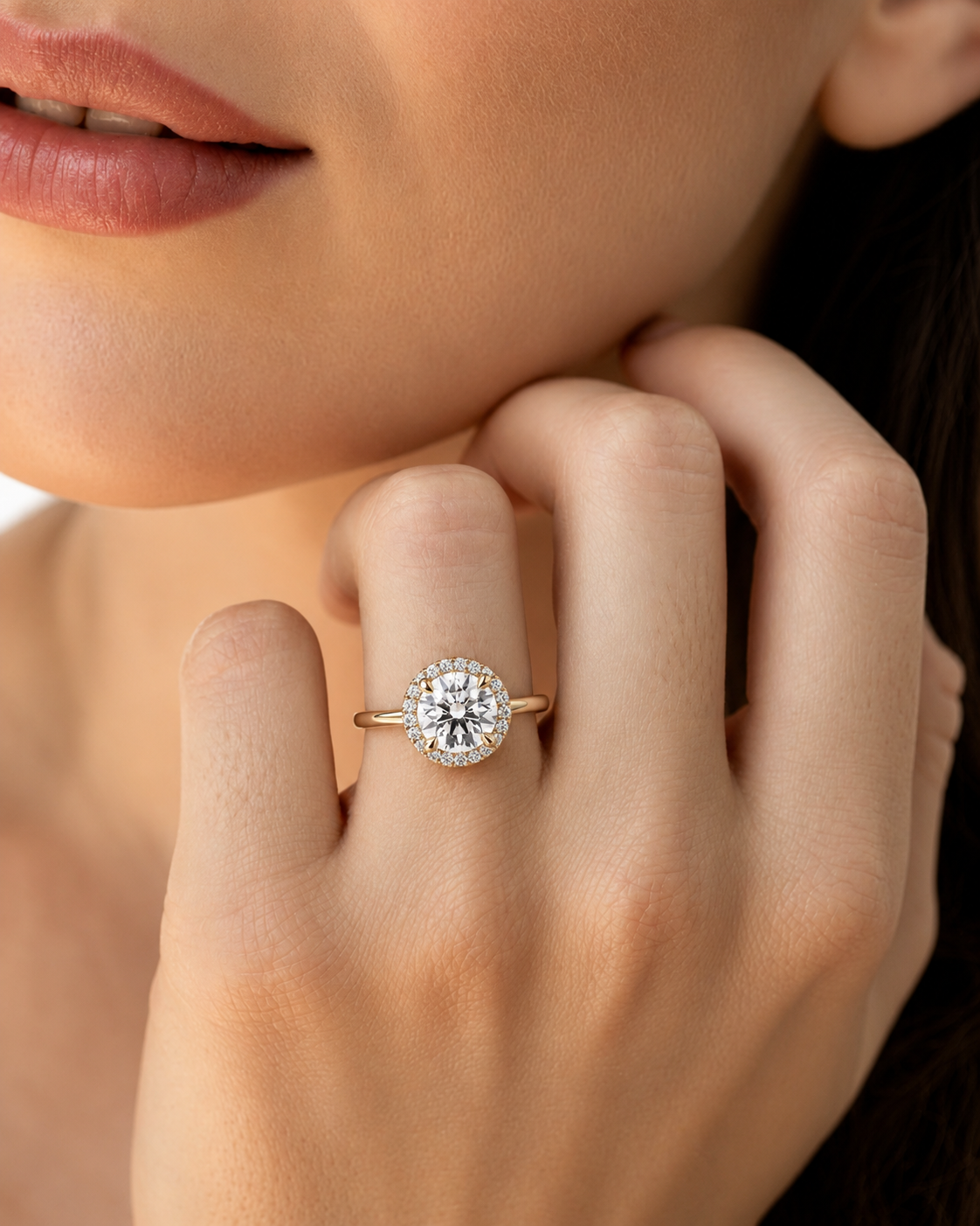 color_10K_YG, color_14K_YG &&	
A close-up lifestyle shot of a woman wearing a gold halo ring with a round-cut diamond on her finger.