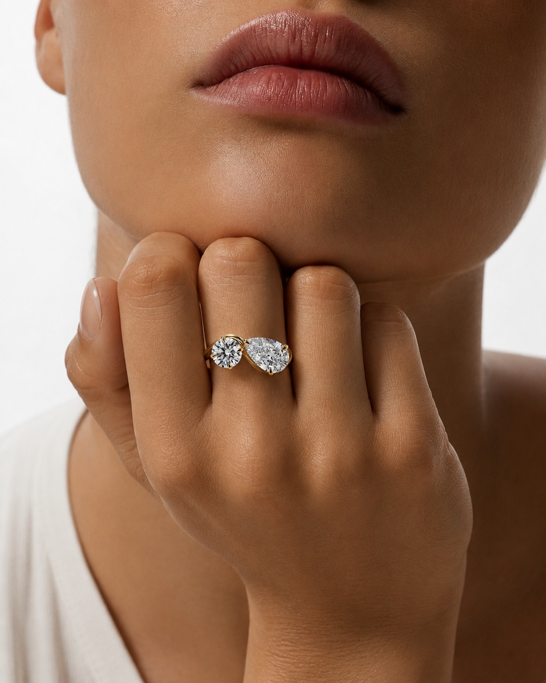 color_10K_YG, color_14K_YG &&	
A close-up lifestyle shot of a model wearing a silver ring with two pear-cut clear gemstones, resting on their finger with their hand near their chin.