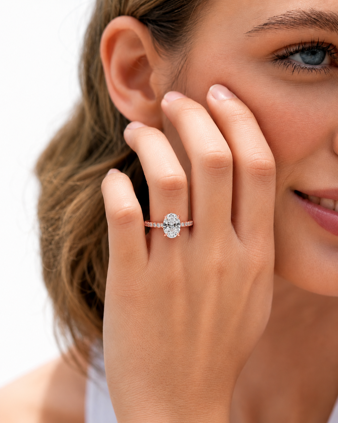 color_10K_RG, color_14K_RG &&	A close-up lifestyle shot of a woman wearing a rose gold engagement ring with a round-cut diamond center stone and small side stones on her finger.
