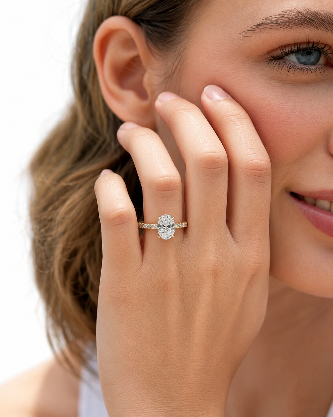 color_10K_YG, color_14K_YG &&	
A close-up lifestyle shot of a woman wearing a silver-toned engagement ring with a round-cut clear center stone and small side stones on her finger, with her hand resting against her cheek.